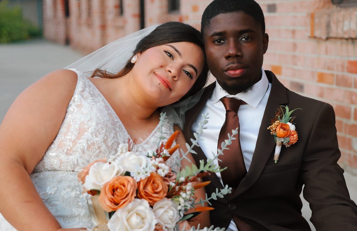 Alejandra leaning against Dontavious in his chocolate suit, beside her orange and white bouquet.