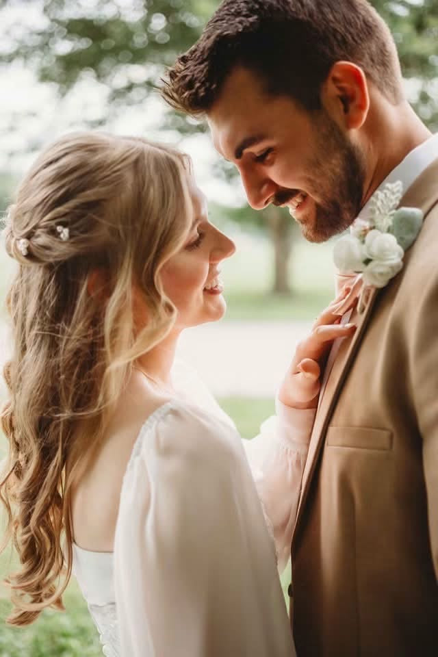 Amanda and Harlen smiling at each other as Amanda holds the lapel of his tan suit.