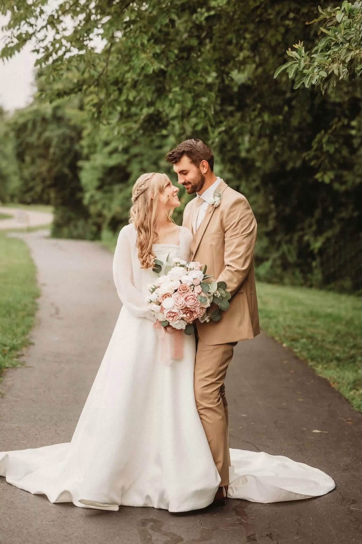 Amanda and Harlen standing on a tree-lined path with a blush-and-white bridal bouquet.