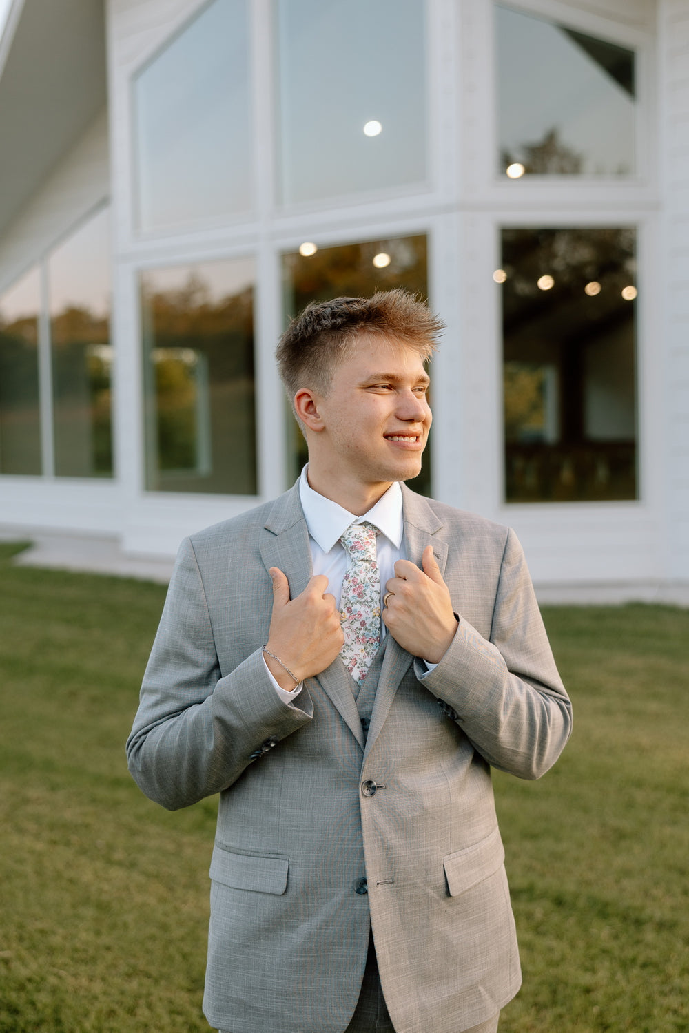 Ryan adjusting the lapels of his gray suit outside a white building.