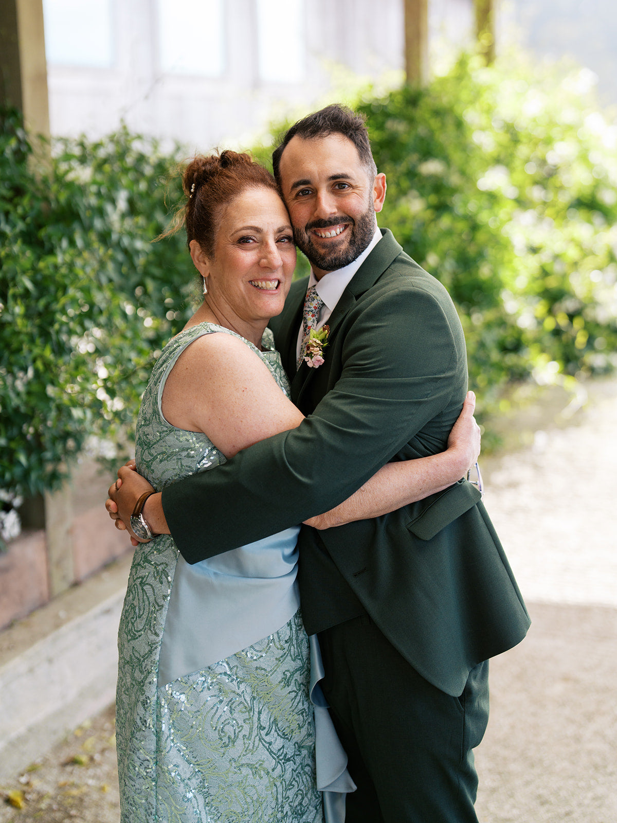Derick in an olive-green suit embracing a woman in a light green embellished dress.