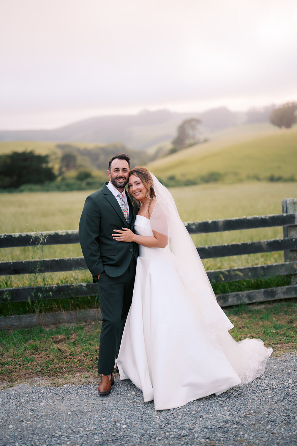 Danielle and Derick beside a wooden fence, showing his olive-green three-piece suit and cognac shoes.