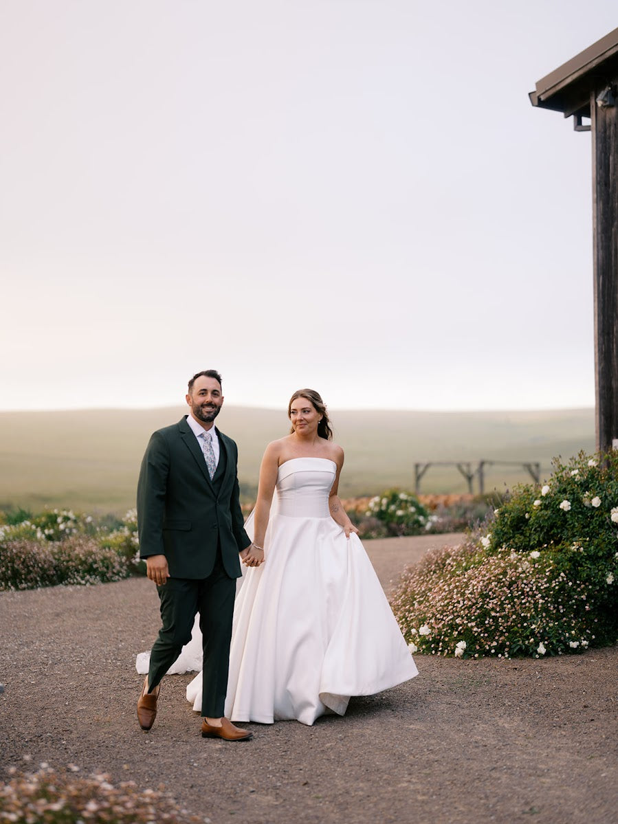 Danielle and Derick holding hands along a gravel path beside a rustic barn.