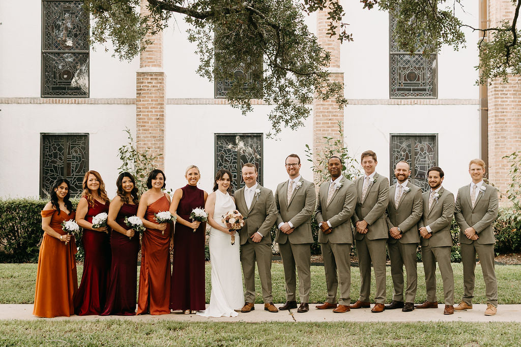 Elisabeth and Kyle with their wedding party in sage suits and autumn-colored dresses.