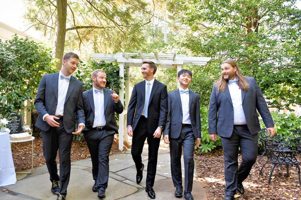 Austin and his groomsmen walking outdoors in charcoal suits and light-blue bow ties.