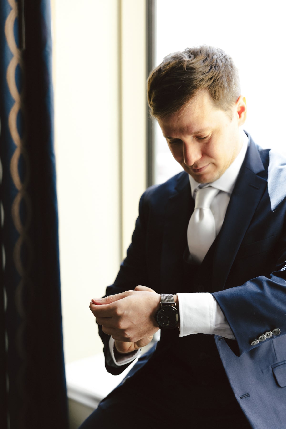 William adjusting his cuff in a navy suit and white tie.
