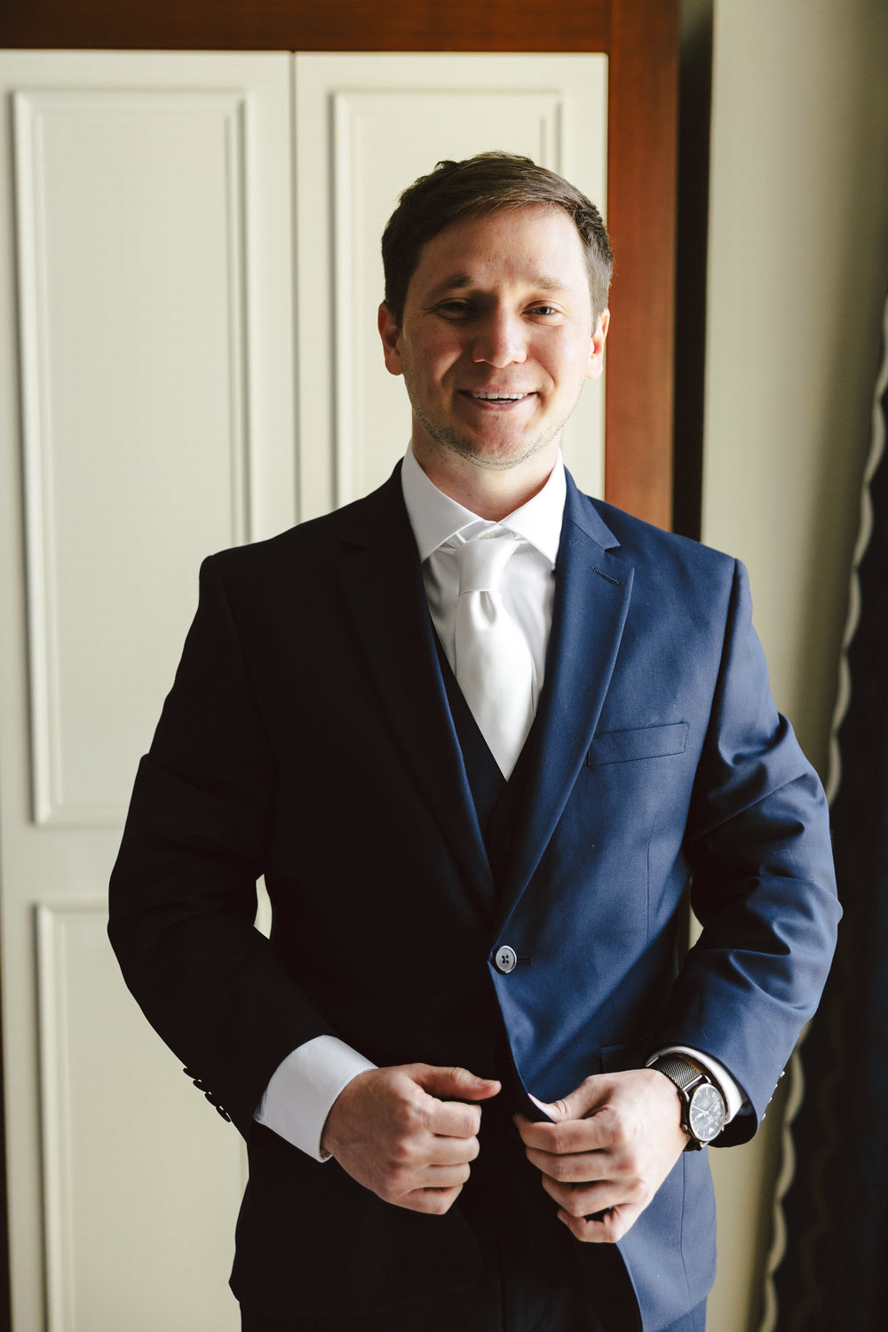 William smiling while buttoning his navy suit jacket.