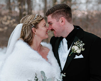 Bride in a white wrap smiling with a groom in a black suit and white tie outdoors.