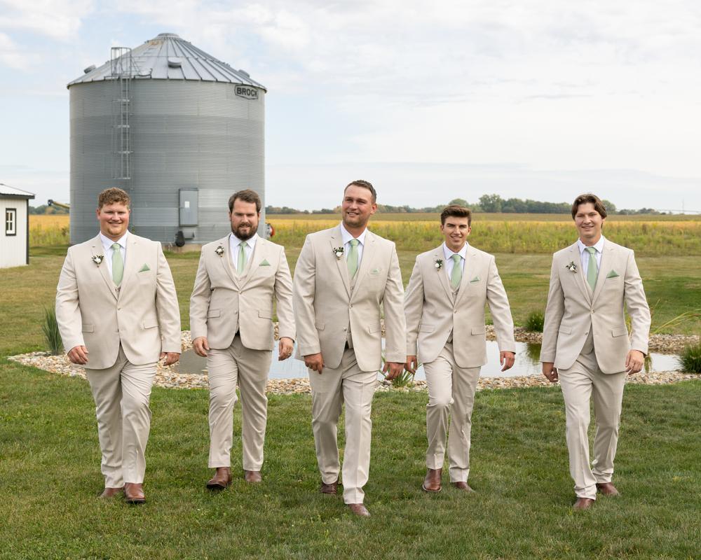 Five men in beige suits standing in a field with a silo in the background
