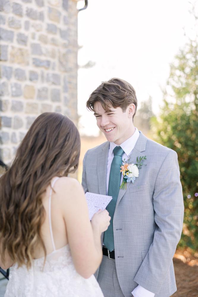 Groom in a gray suit with a floral boutonniere standing next to a bride outdoors.