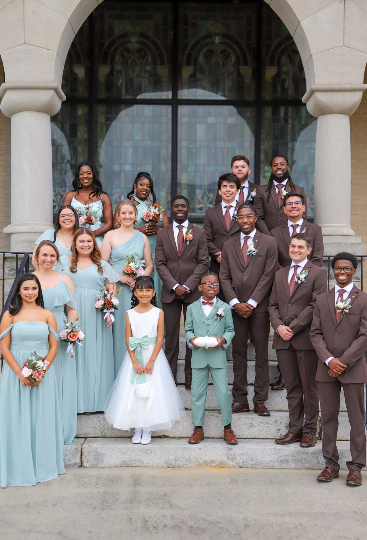 Alejandra and Dontavious with their wedding party in chocolate suits and light-blue dresses on church steps.