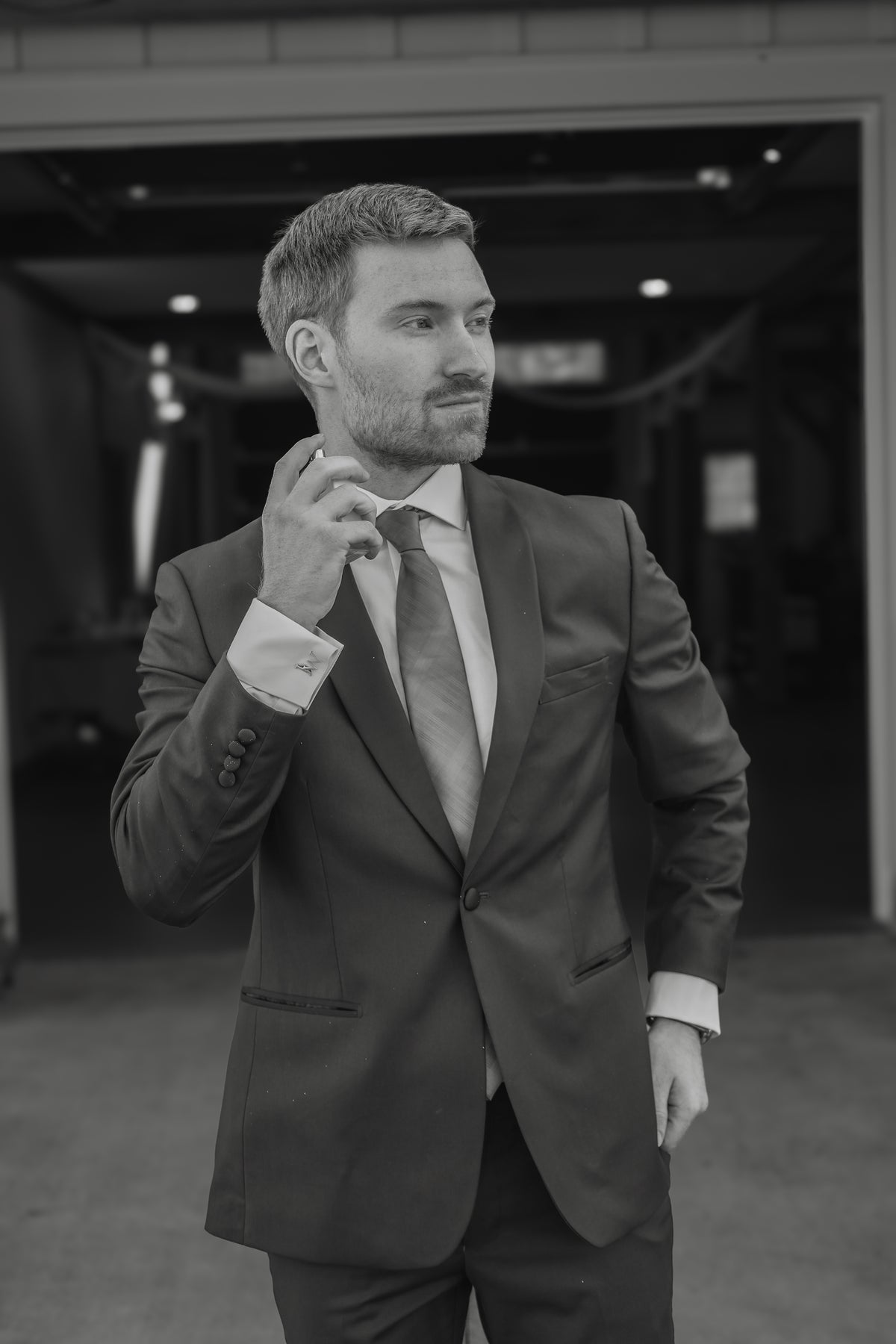 Black-and-white portrait of Jarrett adjusting his wedding suit.