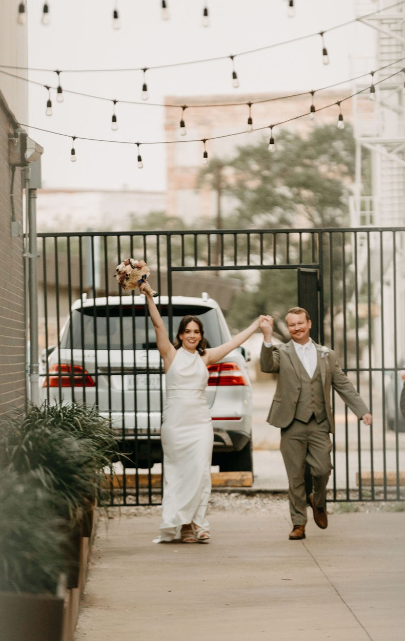 Elisabeth and Kyle walking into their celebration beneath string lights.