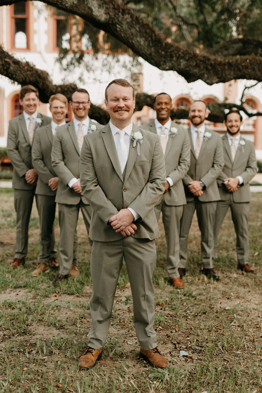 Kyle standing in front of his groomsmen in matching sage suits.