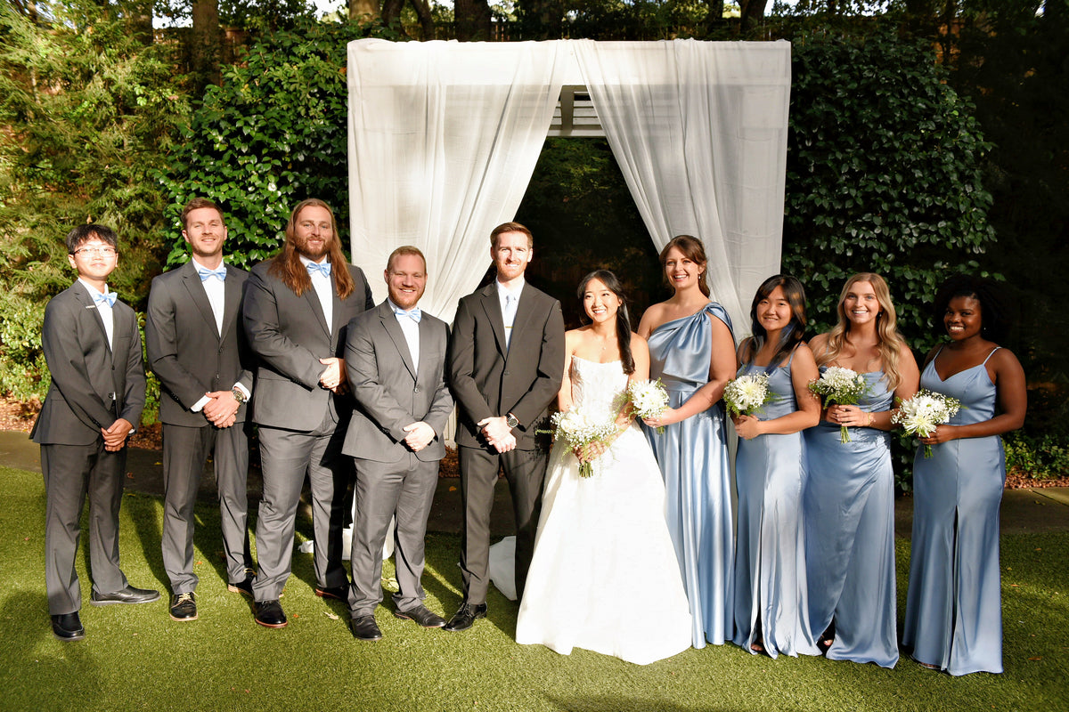 Justine and Austin with their wedding party beneath a white ceremony arch.