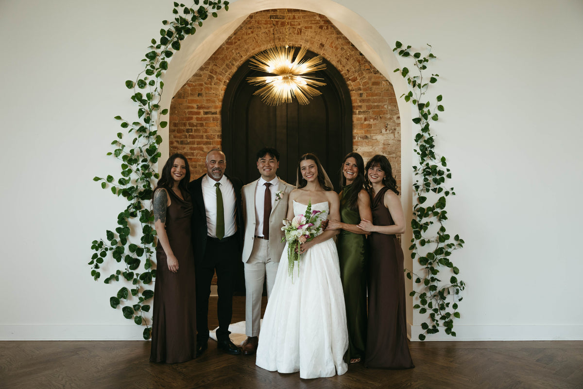 Sophia and Andrew posing with family beneath a vine-framed brick arch.