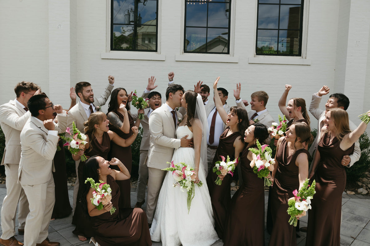 Sophia and Andrew celebrating with their wedding party in tan suits and brown dresses.