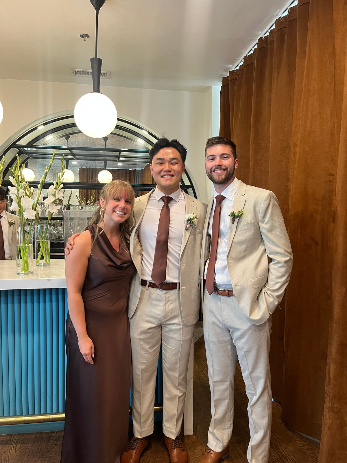 Andrew in his tan suit posing indoors with two guests.
